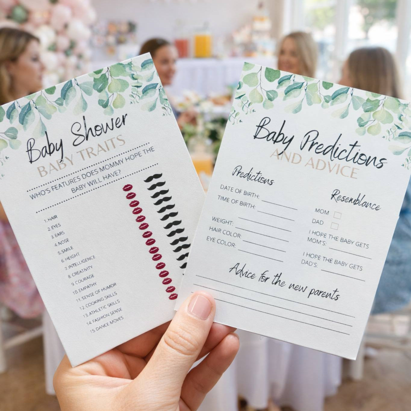 Hand holding baby shower game cards with a blurred background of a baby shower event.